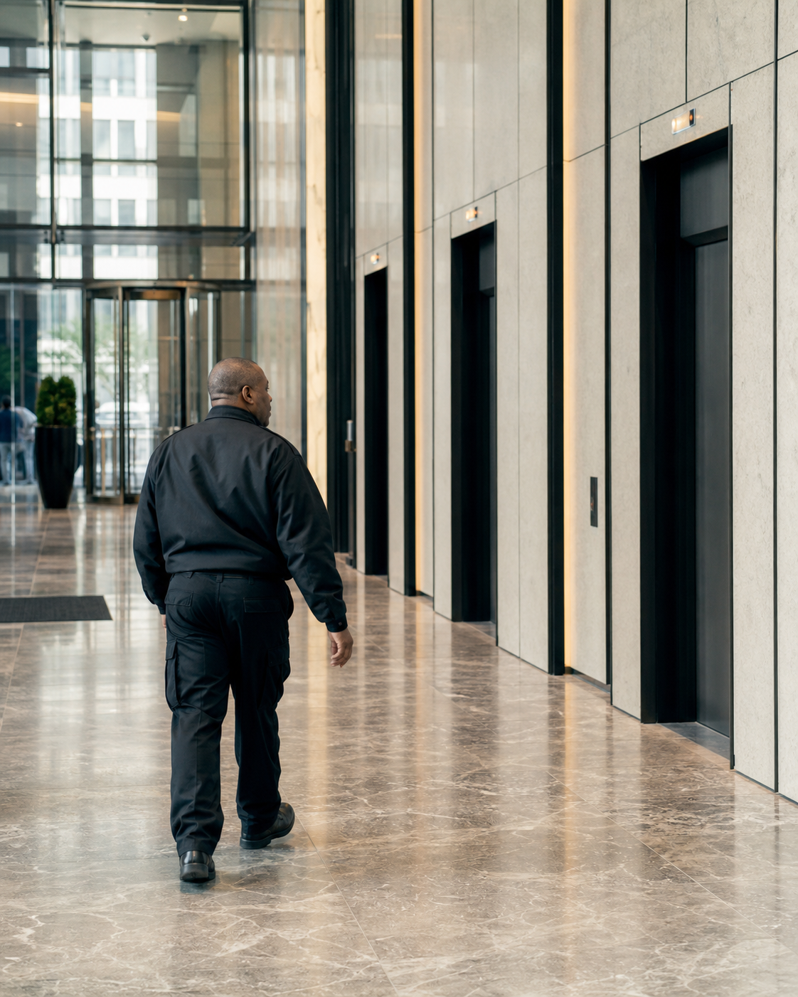 Security officer patrolling an office-building lobby near the elevators and access-controlled doors.
